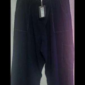 Svarta vida cargopants med kontrastsömmar - Säljer ett par svarta cargopants med bred passform och vita kontrastsömmar. Byxorna har stora fickor på sidorna och är tillverkade i ett lätt tyg som känns luftigt. Perfekta för en chill och avslappnad stil.