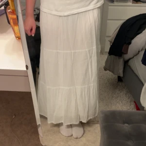 Vit långkjol med volanger - Säljer en superfin vit långkjol med bred resår i midjan och flera volanglager. Kjolen är luftig och flowy, perfekt för varma dagar. Den har en romantisk och bohemisk vibe och är tillverkad i ett tunt, mjukt tyg som känns skönt mot huden.