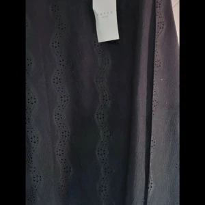 Svart blusmed broderade vågmönster - Svarta blus från Kaffe Curve med vågformade broderade hålmönster ärmar. Blus har en elegant look och är tillverkade i ett lätt tyg som känns luftigt. Perfekta för dig som gillar stilrena detaljer och vill ha något unikt i garderoben.