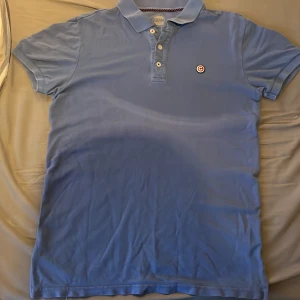 Blå pikétröja från Colmar - Snygg blå pikétröja från Colmar med klassisk krage och tre knappar framtill. Tröjan har korta ärmar och en broderad logga på bröstet. Perfekt för en clean look.