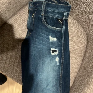 Mörkblå Replay jeans med slitningar - Snygga mörkblå jeans från Replay med slitna detaljer och snygg tvätt. Klassisk femficksmodell med kontrastsömmar och broderade bakfickor. Jeansen har en slim passform och är tillverkade i mjukt denimtyg som sitter skönt hela dagen.