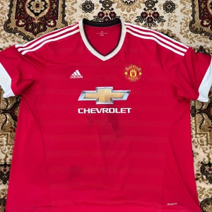 Manchester United Rooney 10 Adidas tröja  - Manchester United matchtröja med Rooney 10 på ryggen. Röd med vita detaljer, Adidas-logga och Chevrolet-sponsor på bröstet. Korta ärmar, klassisk V-ringning och tillverkad i lätt, ventilerande climacool-material. Perfekt för dig som älskar fotboll och United.