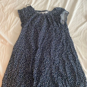 Blommig marinblå kortklänning - Supersöt marinblå kortklänning med små vita blommor över hela tyget. Klänningen har korta ärmar och en avslappnad passform med resår vid halsen. Perfekt för varma dagar och sätta över sig på stranden. Pris kan diskuteras.