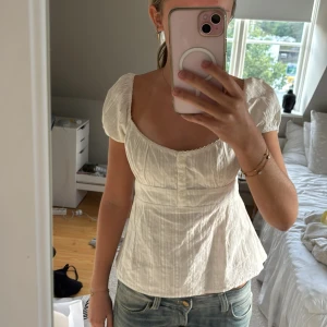 Vit blus med puffärm från Nelly - Supersöt vit blus från Nelly med puffiga korta ärmar och knappar framtill. Blusen har en lätt v-ringad halsringning och har smock i ryggen. Priset kan diskuteras.
