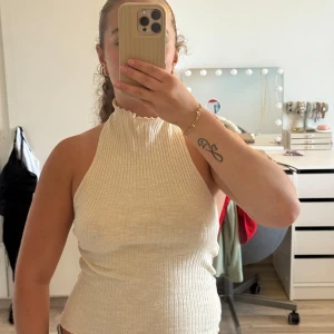 Ribbad halterneck topp i beige - Toppen är ärmlös och har en bred resårdetalj baktill som håller den på plats. 