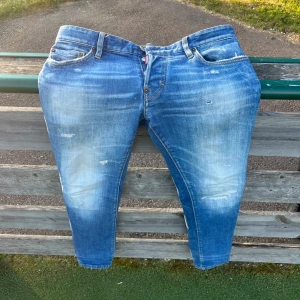 Blå Dsquared2 jeans med slitningar - Säljer ett par blå jeans från Dsquared2 i storlek 46. Jeansen har en snygg tvätt med slitna detaljer och ljusa partier framtill och baktill. Klassisk femficksmodell med raka ben och coola slitningar för en trendig look.