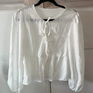 Vit blus med knyt och volang SHEIN oanvänd  - Supersöt vit blus med långa puffärmar, knyt framtill och volang nedtill. Tunt, lätt strukturerat tyg som ger en luftig känsla. Perfekt för dig som gillar romantisk och trendig stil. Passar lika bra till jeans som kjol. Aldrig använd därmed i nyskick! Storlek L