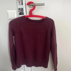 Vinröd stickad tröja från Hollister - Vinröd stickad tröja från Hollister i storlek M. Klassisk rund halsringning och diskret logga på bröstet. Mjuk och skön, perfekt för kyliga dagar. Långärmad modell med enkel och stilren design.