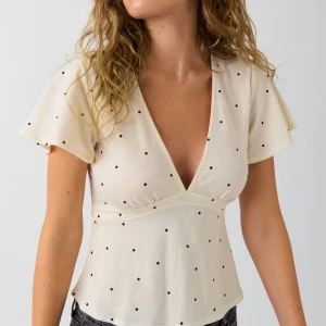 Prickig omlottopp - Supersöt ljusbeige omlottopp med svarta prickar från Gina Tricot. Djup v-ringning, korta vida ärmar och knyt i ryggen för en snygg passform. Perfekt till jeans eller kjol för en trendig look.