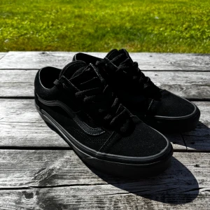 Svarta Vans Old Skool sneakers - Klassiska Vans Old Skool sneakers i helsvart mocka och canvas. Ikonisk sidoswosh i svart och den typiska gummisulan i orange undertill. Perfekta för en streetwear-look.
