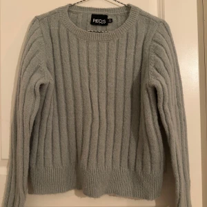 Ljusgrå ribbstickad tröja från Pieces - Supermjuk ljusgrå/ grön ribbstickad tröja från Pieces. Klassisk rund halsringning och långa ärmar. Perfekt för lager-på-lager och chill dagar. Snyggt ribbat mönster som ger en clean look.