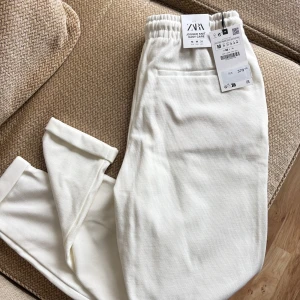 Vita joggerbyxor från Zara - Snygga vita joggerbyxor från Zara med elastisk midja och mjukt stickat material. Byxorna har en relaxed passform och praktiska fickor. Helt nya, kommer i mycket bra skick.