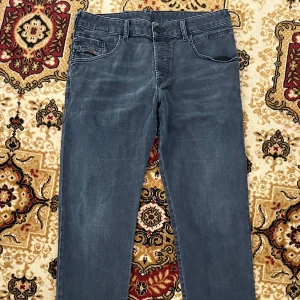 Diesel Mörk Grå jeans, straight fit - Säljer ett par mörk grå jeans från Diesel i rak modell. Jeansen har klassisk femficksdesign, knappgylf och diskreta slitningar för en cool look. Materialet är mjukt och stretchigt för extra komfort. Perfekta för dig som gillar stilrena och tidlösa jeans.