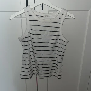 Randig vit linnetopp från Cubus - Säljer en fräsch vit linnetopp från Cubus med svarta horisontella ränder. Toppen är ärmlös med klassisk rund halsringning och tillverkad i mjuk bomull med lite stretch för extra komfort. Perfekt för en chill och stilren look.