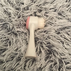 Dubbelverkande sminkborste vit/rosa - Säljer en dubbelverkande sminkborste i vit plast med ett handtag som är lätt att greppa. Ena sidan har täta, mjuka borsthår för applicering av smink, andra sidan har en rosa silikonpad perfekt för rengöring eller exfoliering. Passar till både foundation och rengöring.