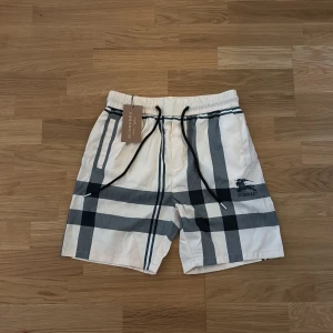 Vita Burberry shorts - Snygga vita Burberry shorts med klassiskt rutigt mönster i svart och grått. De har elastisk midja med svart snörning och Burberry-logga tryckt på benet. Hör av dig om du har några frågor. Pris kan diskuteras vid snabb affär 