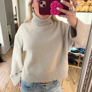 Beige stickad polotröja - Säljer en beige polotröja med bred och ribbad krage samt breda, ribbstickade muddar vid ärmslut och nederkant. Tröjan är stickad och har en loose passform som ger en chill vibe. Perfekt att matcha med jeans för en enkel och snygg look.