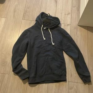 Pier One hoodie - Säljer en mörkblå hoodie från Pier One med klassisk känguruficka och vit snörning i huvan. Tröjan har långa ärmar och är gjord i mjuk bomull, perfekt för chill dagar. Enkel och stilren design som funkar till jeans eller joggers.