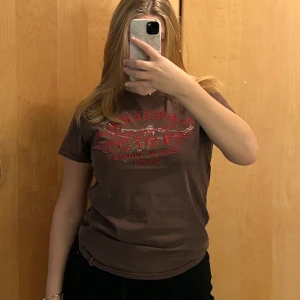 Brun t-shirt Jack & Jones med tryck - Säljer en brun t-shirt från Jack & Jones med rött och vitt tryck framtill. Texten 'GUILTY 1975 Rock for Freedom Concert' ger en cool vintagekänsla. T-shirten har rund hals och är kortärmad, perfekt till jeans eller shorts.