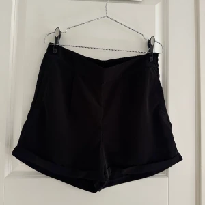 Svarta shorts från Vero Moda - Svarta shorts från Vero Moda med elastisk midja och avslappnad passform. De har en enkel design med diskreta fickor i sidorna och uppvikta benslut. Perfekta för varma dagar när du vill ha något bekvämt och stilrent.