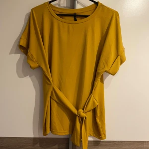 Gul kortärmad topp med knyt - Snygg gul topp med korta ärmar och trendig knytning i midjan. 