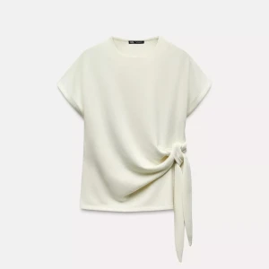 Vit knyttopp från Zara - Säljer en vit stickad T-shirt från Zara i storlek M. Toppen har korta ärmar, rund halsringning och en snygg knytdetalj i sidan. Sitter som en s. Endast använd 2 gånger.