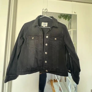 Svart jeansjacka  - Snygg svart jeansjacka från Kappahl med klassisk krage, silverfärgade knappar och två bröstfickor med lock. Jackan har raka linjer och är tillverkad i denim, perfekt för dig som gillar en stilren och tidlös look. Storlek 140💕