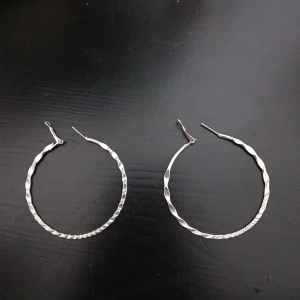 Stora silvriga hoops örhängen - Säljer ett par stora, runda hoops i silverfärg med vriden och hamrad yta som ger en cool och modern look. Perfekta för att lyfta vilken outfit som helst. Lätta att bära och stängs med klassiskt lås. Supertrendiga och snygga till allt. Har aldrig använts men har tyvärr inte kvittot och kom gärna med prisförslag😇