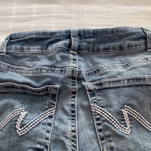 Blå jeansshorts från Nelly - Snygga blå jeansshorts från Nelly med råa kanter och dubbla knappar framtill. Shortsen har klassiska bakfickor med vit broderad detalj och en avslappnad passform. Säljer då de inte passar mig. Använda 1-2 gånger och inga tecken på användning.