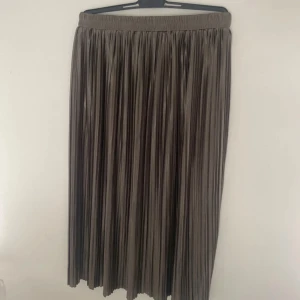 Plisserad långkjol i satin från SHEIN - Snygg plisserad långkjol från SHEIN i glansigt satinliknande material. Kjolen är mörk beige med en lätt skimrande finish och har resår i midjan för extra komfort. Perfekt för dig som vill ha en trendig och flowy look.