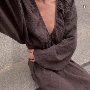 Brun långklänning med v-ringning från Nakd - Helt oanvänd brun långklänning med djup v-ringning och långa ärmar. Klänningen har en loose passform och är erfekt för dig som gillar avslappnad och stilren look. 