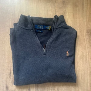 Mörkgrå half zip tröja Polo Ralph Lauren - Mörkgrå ribbstickad tröja från Polo Ralph Lauren i storlek XS. Klassisk half zip med liten broderad logga på bröstet. Tröjan har hög krage och är perfekt för lager-på-lager. Snygg och stilren modell som funkar till det mesta.