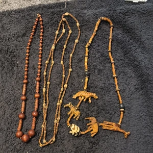 Bruna trä- och pärlhalsband vintage  - Tre unika halsband i trä och pärlor, varav ett har handgjorda djurfigurer som elefant, giraff och noshörning. De har olika former av bruna och beige pärlor, och ger en bohemisk och naturlig vibe. Perfekt för dig som gillar detaljer och naturinspirerat.