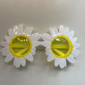 Solglasögon i form av prästkragar - Unika solglasögon med stora vita prästkrage-blommor runt de runda gula glasen. Ramen är vit och plastig, och linserna är klargula. Perfekta för att sticka ut på festival eller sommarhäng!