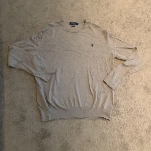  tröja  Polo Ralph Lauren cashmere  - Snygg grå långärmad tröja från Polo Ralph Lauren med klassisk rund hals och broderad logga på bröstet. Tillverkad i mjuk bomull som känns skön mot huden. Perfekt för en clean och stilren look.