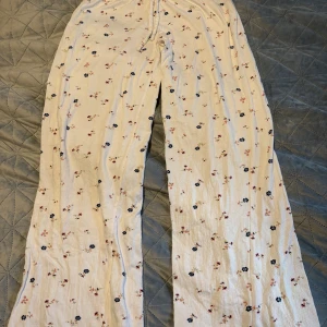 Blommiga vita manchesterbyxor - Säljer ett par vita manchesterbyxor med blommigt mönster i rosa och blått. Byxorna har raka ben och en avslappnad passform, perfekta för dig som gillar en chill och söt stil. Materialet är mjukt och ger en skön känsla. Passar dig som vill sticka ut med ett gulligt print.