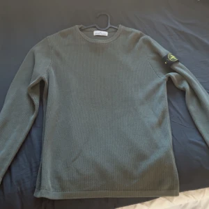 Grön stickad tröja från Stone Island - Säljer en grön stickad tröja från Stone Island i storlek L. Tröjan har lång ärm och klassisk rund hals. På vänster ärm sitter den ikoniska Stone Island patchen i svart och gult. Pris ej ristat i sten.