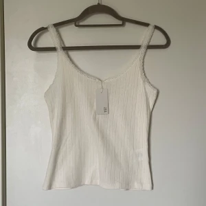 Vit spetskantad linnetopp 157 - Supersöt vit linnetopp från Lager 157 i storlek S.  Toppen har tunna spets axelband (ej justerbara) och spetskant runt halsringningen samt  hålmönster i ränder längst med tyget. Säljs med tag kvar! Då den är för stor och jag har inte hunnit returnera🩷ordinarie pris är 80 kr