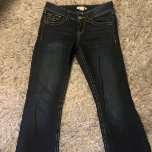 Mörkblå jeans från Gina Tricot - Snygga mörkblå jeans från Gina Tricot med kontrastsömmar och coola fickdetaljer med lock och knapp bak. Klassisk femficksmodell och rak passform. Perfekta för dig som gillar stilrena jeans med lite edge. Passar dig som vill ha en tidlös look.