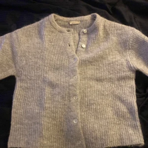 Grå stickad kofta från Gina Tricot - Mysig grå stickad kofta från Gina Tricot i storlek XS. Koftan har en klassisk design med knappar framtill och ribbad struktur. Perfekt för kyliga dagar och enkel att matcha med olika outfits.