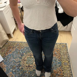 Vit linnetopp med spetsdetaljer från Svea - Säljer en söt vit linnetopp från Svea med svarta spetsdetaljer längs kanten. Toppen har knappar framtill och tunna axelband. Perfekt för varma dagar eller som ett lager under en tröja.