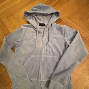 Ljusblå hoodie från Juicy Couture - Säljer en mjuk och stilren ljusblå hoodie från Juicy Couture. Den har en dragkedja framtill och en broderad logga på bröstet. Perfekt för en avslappnad look med en touch av lyx. 🩵