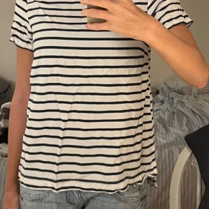 Randig t-shirt - Säljer en klassisk randig t-shirt i svart och vit. Den har korta ärmar och en bekväm passform. Perfekt för en avslappnad stil. Hör av dig vid intresse!