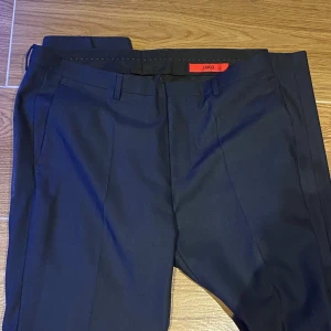 Kostymset från Hugo Boss - Säljer stilren vit skjorta, mörkblå kavaj och byxor från Hugo Boss i regular fit. Skjortan har långa ärmar och knappar framtill. Perfekt för en klassisk look och enkel att stryka. Passar bra till både formella och avslappnade tillfällen. Köpt på hede fashion outlet i Kungsbacka för runt 6-7 tusen kr