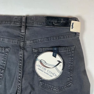 Grå jeans från Jacob Cohën - Snygga grå jeans från Jacob Cohën med klassisk femficksdesign och knappgylf. Byxorna har en stilren look med subtila detaljer och är i perfekt skick! Alla Jacob Cohën jeans är L34" längd. W26 men sitter som 28. 