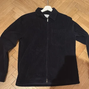Mörkblå manchesterjacka från Bläck - Säljer en stilren svart manchesterjacka från Bläck. Jackan har en dragkedja framtill och en bröstficka.  Nypris 1599kr, använt 3 gånger