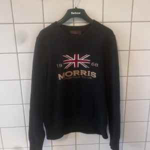Marin blå tröja från Morris - Snygg svart tröja från Morris med ett stort tryck av Union Jack och texten 'Morris Sporting Club' på framsidan. Tröjan har långa ärmar och ribbade kanter vid hals, ärmslut och nederkant. Perfekt för en stilren look. Nästan helt ny 