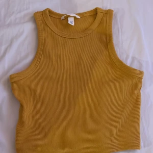 Gul ribbad linnetopp från H&M - Säljer en snygg gul ribbad linnetopp från H&M. Perfekt för varma dagar med sin ärmlösa design och bekväma passform. Ett måste i garderoben för en stilren look. 🌼