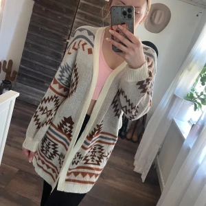 Beige kofta med mönster - Säljer en mysig beige kofta med brunt och grått mönster. Koftan har långa ärmar och en öppen design utan knappar. Perfekt för kyliga dagar och ger en avslappnad stil. Finns en liten fläck på ärmen se bild 3. Har ej testat med vanish. 