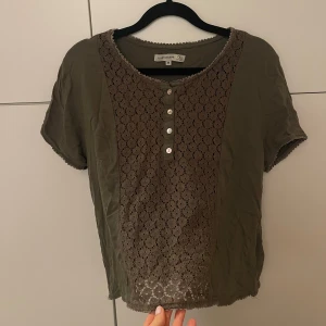 Blus - Säljer en grön topp med spetsdetaljer framtill och knappar. 